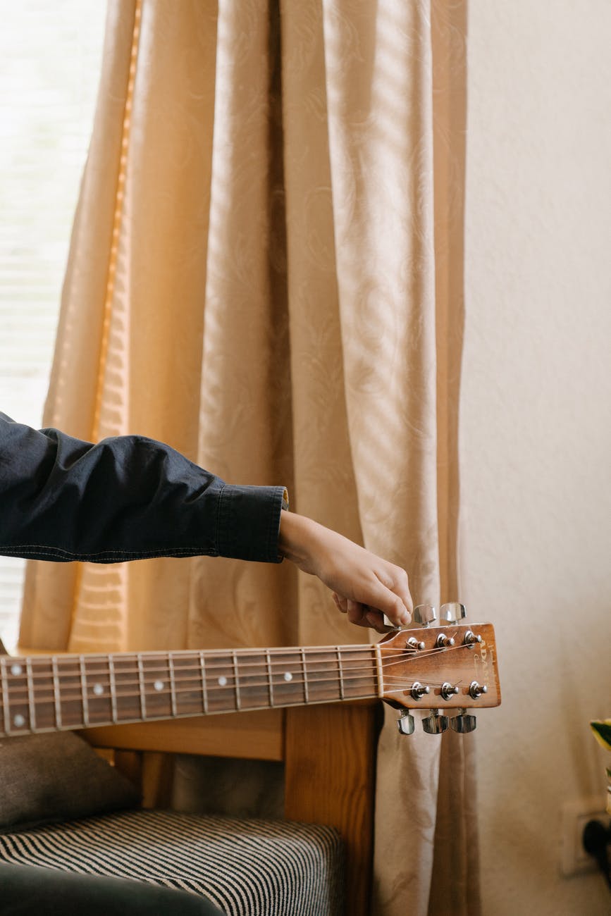 person playing guitar near brown curtain